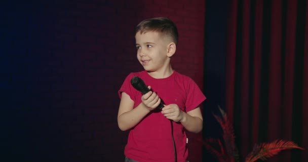 ステージにマイクを持った小さな男の子 才能ショーのオーディションにマイクを持っている面白い小さな子供 コンサートでのユーモラスな子供の即興 マイクを持ったアーティストの少年がステージで笑いを止める — ストック動画