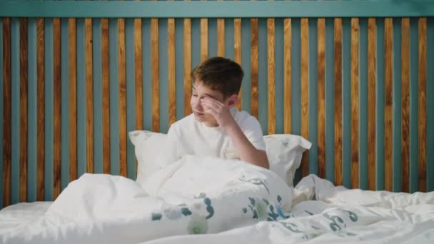 小さな男の子が消極的に目を覚まし 伸ばし 手で目をこすり しるし ヨーンと寝床に落ちる 子供には休息が欠けていて 起き上がる努力をしています 健康的な睡眠の概念 — ストック動画