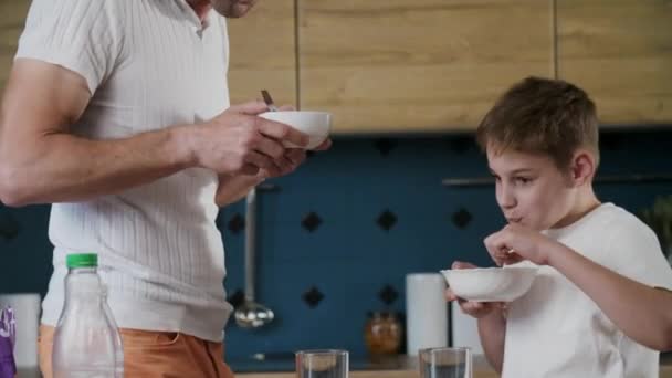 一个友好的父子家庭 手拿着碗 站在厨房里吃饭 一位父亲和孩子们分享了一个美味配方的想法 互助的概念 射击方式 — 图库视频影像