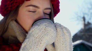 Genç ve güzel bir kadın sıcak içkinin tadını çıkarıyor. Termosun içinde sıcak şarap. Eldivenli mutlu gezgin kız termostan çay içiyor. Winter City Parkı. Yüksek kalite 4k görüntü