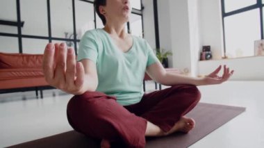 Yaşlılıkta hoş ve kullanışlı bir eğlence anlayışı. Yaşlı kadın evde yoga egzersizi yapıyor. Olgun kadınlar meditasyon yapar. Kameraya bakar ve gülümser. Yüksek kalite 4k görüntü