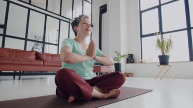 Yaşlı kadın evde yoga egzersizi yapıyor. Olgun kadınlar meditasyon yapar. Ellerini birleştir ve gülümse. Güne iyi duygularla başla. Yüksek kalite 4k görüntü