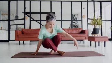 Yaşlı kadın evde yoga egzersizi yapıyor. Olgun kadınlar meditasyon yapar. Yatağa oturur, pencereden dışarı bakar ve dinlenecek vakti olduğuna sevinir. Yüksek kalite 4k görüntü