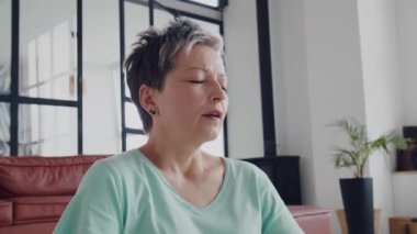 Yaşlı kadın evde yoga egzersizi yapıyor. Olgun kadın kas, boyun, eller ve kafa hareketleriyle egzersiz yapmaya hazırlanıyor. Yüksek kalite 4k görüntü