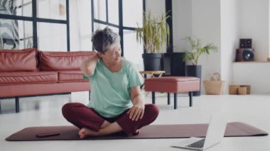 Yaşlı kadın evde yoga egzersizi yapıyor. Olgun kadın kas, boyun, eller ve kafa hareketleriyle egzersiz yapmaya hazırlanıyor. Yüksek kalite 4k görüntü