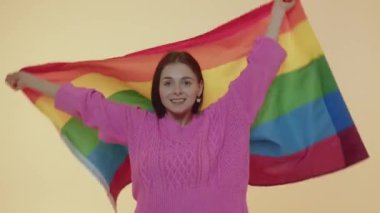 Özgürlüğün sembolü olarak çok renkli LGBT bayrağı gösteren yetişkin bir protesto kadını. Cinsiyet ayrımcılığını durdurun. Hoşgörülü ol. Bej renkli arka planda izole edilmiş gökkuşağı bayrağıyla el kaldıran genç bir kız.