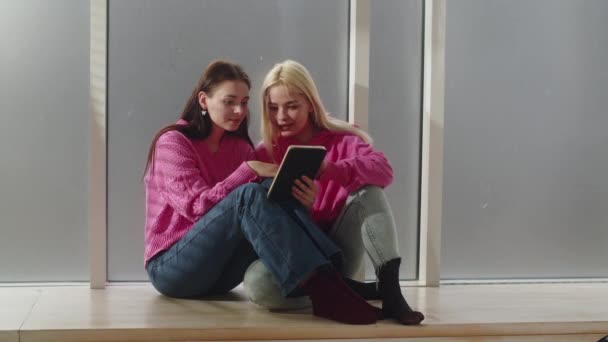 2人の若いガールフレンドが床に座り 数学の試験の前にタブレットを使用しています レズビアン ガールズはタブレットを使ってビデオを見ている 一緒に座って宿題をするかわいい女性のカップル — ストック動画