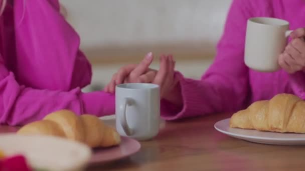 关起来年轻的女同性恋者爱抚 喝茶与羊角面包在约会 保持人际关系的和谐 在家里喝咖啡时 穿着粉色套头毛衣的妇女手挽手 爱情故事 — 图库视频影像