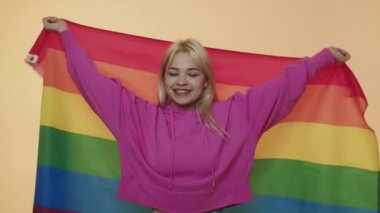 Özgürlüğün sembolü olarak çok renkli LGBT bayrağı gösteren yetişkin bir protesto kadını. Hoşgörülü ol. Pembe kapüşonlu genç bir sarışın el kaldırıyor ve bej rengi bir bayrakla gökkuşağını sarıyordu.