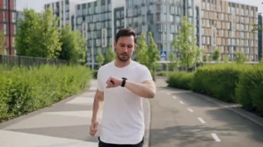 Genç, konsantre bir sporcu sabah yürüyüşünü kaldırımda yapar ve saati kontrol eder. Bir atlet hafif koşuya başlar ve şehir parkındaki koşuyu hızlandırır.