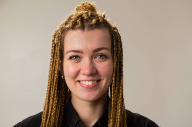 Saçları katmanlı ve örgülü bir kadın mutlu bir şekilde gülümsüyor, gözleri neşeyle parıldıyor. O, çene çizgisi ve kirpiklerini vurgulayan siyah bir gömlek giyiyor..