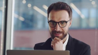 Bilgisayar ekranına bakarak online ticaret piyasasının dijital verilerini analiz eden olgunlaşmış bir işadamı. Büyük ofiste gözlüklü genç adam internette çalışıyor ve gülümsüyor.