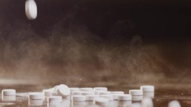 Bir avuç dolusu beyaz ilaç kahverengi bir yüzeye düşer. İlacın bir mikro parçacık sisi havaya karışıyor. Hap düşer ve masadan seker. Yavaş çekim modu. Yüksek