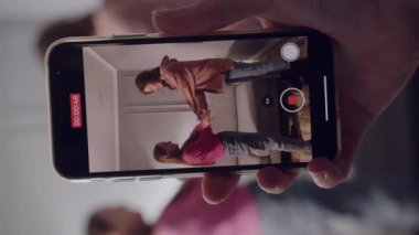 Bir kadın fotoğrafçı elinde bir akıllı telefon, bir video ve iki kızın fotoğrafını çekiyor. Gülümseyen, neşeli, neşeli ve enerjik bayanlar el ele tutuşup poz vermek için kameraya bakıyorlar. Kapat