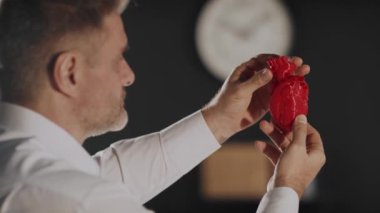 Grafik tasarımcısı insan çene kemiğinin plastik 3D baskılı modelini yandan tutuyor ve görüyor. Laptop ekranında kırmızı renkli bir kalp resmi. Protezler için biyobasım organları konsepti ve