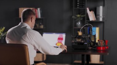 Grafik tasarımcı bir adam dizüstü bilgisayar kullanır, kırmızı ve sarı renkli vazo çizimi yapar ve geometrik formda bir vazo yapar. Bir 3D yazıcı otomatikleştirilmiş otonom işlemde çalışır. Konsept: