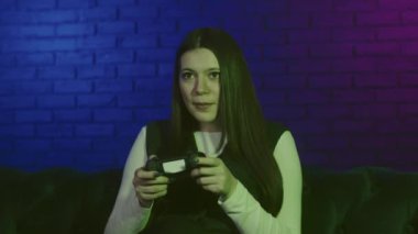 Video oyunları bağımlılığı kavramı. Yetişkin genç bir kadın, duygusal olarak joystick ile oynuyor. Oyun üyeleri arasındaki şampiyonluğu kazandığını görünce heyecanlanan kız yumruklarını kaldırdı. Oyunu salonda kazan.