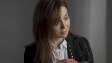 Ofis müdürü kadın ofisinde şık gözlüklerini takıyor. Formalite içinde çekici ve kendine güvenen bir iş kadını. Kendine güvenen iş kadınının yavaş çekim görüntüsü. Şık gözlüklerini çıkar. Yüksek