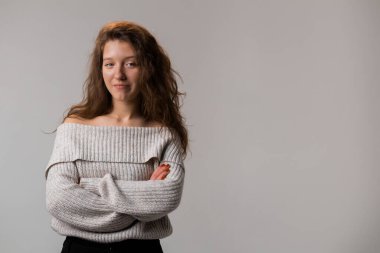 A woman in a grey sweater is standing with her arms crossed, one hand on her elbow and the other on her waist, gesturing confidence at the event.