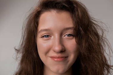 A close up of a womans face with layered hair, messy hair, a happy smile, and eyelashes. Her forehead, nose, cheeks, and jaw are visible, as she gestures happily