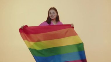 Özgürlüğün sembolü olarak çok renkli LGBT bayrağı gösteren yetişkin bir protesto kadını. Cinsiyet ayrımcılığını durdurun. Hoşgörülü ol. Bej renkli arka planda izole edilmiş gökkuşağı bayrağıyla el kaldıran genç bir kız.