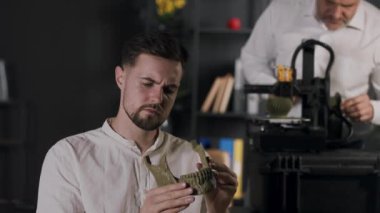 Genç bir araştırma asistanı el ele tutuşup insan çene kemiğinin haki renkli plastik modelini görüyor. Orta yaşlı bir makine mühendisi dijital kalibreler kullanır ve 3D yazıcının çalışmasını özelleştirir