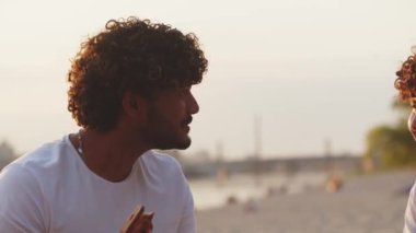 İki erkek sahilde kızlar hakkında konuşuyor. En iyi arkadaşlar arasındaki entelektüel savaş. Kıvırcık saçlı öğrenciler sahilde konuşuyor. Esprili hikayeler ve fıkralar anlatırdı. Yüksek kalite 4k görüntü