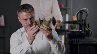 Orta yaşlı bir bilim adamı insan çene kemiğinin haki renkli plastik modelini tutuyor ve dişlerin gücünü kontrol ediyor. Genç bir araştırma asistanı 3D yazıcının çalışmalarını gözlemliyor, tablet kullanıyor ve...
