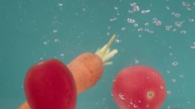 Turkuaz arka plandaki sebzeler suya batar ve kabarcıklar oluşturur. Havuç ve domatesler dibe batar ve yere yatar. Kırmızı biber ve yeşil soğanlar yüzeye çıkar. Hazırlık konsepti