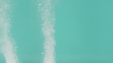 Turkuaz arka planda bulunan beyaz renkli haplar kabın dibinde yatar ve suda çözünerek su yüzeyine yükselen kabarcıklar ve toz oluştururlar. Test konsepti