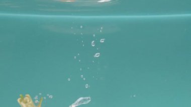 Tek bir havuç türkuaz bir zemin üzerinde suya batar, kabarcıklar oluşturur ve ekseni etrafında bir girdap gibi döner. Sağlıklı vejetaryen yemeği ve yemeği kavramı. Yavaş çekim kipi