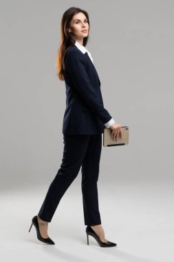 Resmi giyinmiş, evrak çantası taşıyan profesyonel bir kadın, takım elbisesiyle rahatça yürüyor..
