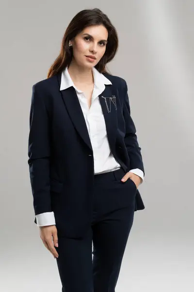 Kadın beyaz bir gömlek giymiş, saçı zarif bir şekilde şekillenmiş. Gömleğin yakası boynunu çerçeveliyor ve kolları nazikçe kollarına düşüyor, belini vurguluyor..