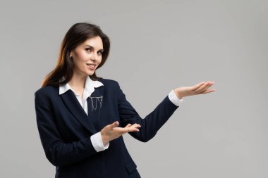 İş elbisesi giymiş bir kadın profesyonel bir jest yaparak elini uzatıyor. Yapılandırılmış ceketin altında gömleğini ve gömleğini gösteriyor..