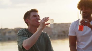 İki genç adam şişelerde kokteyl içip sahilde gülüyorlar. Öğrenciler için dinlenme ve parti zamanı. Elma suyu içen iki kişi ile bira içen iki kişi arasında komik bir diyalog. Yaz zamanı anları. Yüksek kalite