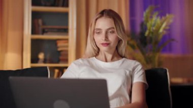 Akşamları, genç bir kadın evdeki rahat kanepede laptopunu kullanıyor, sıcak bir ortam ile çevrili.
