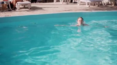 Bir kadın, güneşli ve güneşli bir günde, bir otel havuzunda yüzerken ve serin suyun keyfini çıkarırken görülüyor..