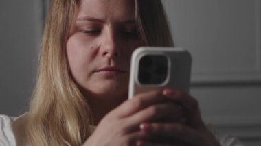 Sarı saçlı genç bir kadın akıllı telefonuna odaklanmış, modern iletişim teknolojisini sergiliyor.