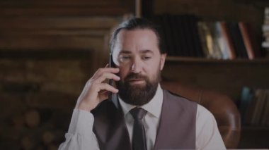 İş adamı ofis ortamında cep telefonuyla konuşuyor, resmi kıyafetlerle mesleki konuları tartışıyor..