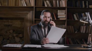 Takım elbiseli iş adamı belgeleri gözden geçirir, telefonla konuşur, işine odaklanır ve ofiste önemli kararlar verir.