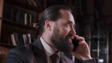 Takım elbiseli profesyonel bir işadamı ofisinde telefon görüşmesi yapıyor, kitaplık geçmişi var..