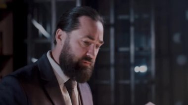 Takım elbiseli bir iş adamı modern ofis ortamındaki belgeleri analiz etmeye yoğunlaşır.