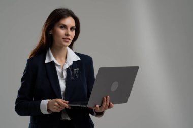 Resmi giyinmiş beyaz yakalı bir işçi, bir şirket etkinliğinde dizüstü bilgisayarını kolunda tutarken jest yapıyor..