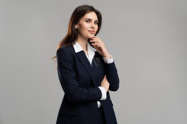 İş elbisesi giymiş bir kadın, elleri çaprazlanmış, elleri çenesinde ve resmi giysiler içinde duruyor. Elbise, ceket ve tasma da dahil..