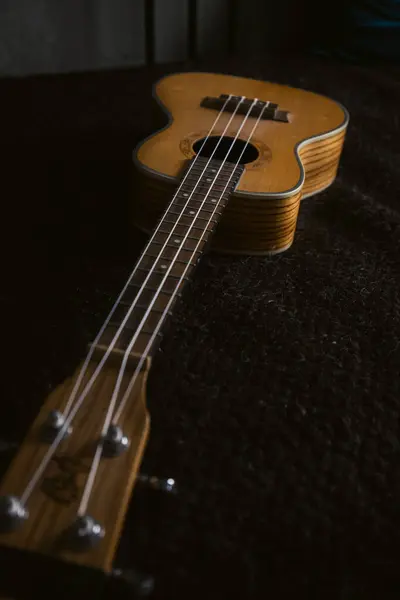 Koyu renk bir arkaplana yerleştirilmiş ahşap bir ukulelenin yakın plan görüntüsü, tellerini ve dokusunu vurguluyor..