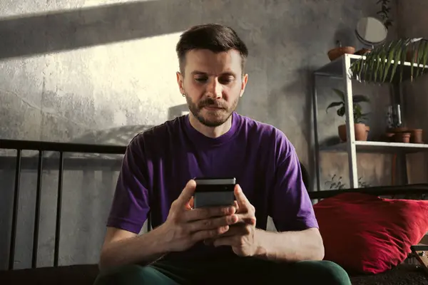 Sakallı genç bir adam sakince akıllı telefonunu şık, çağdaş bir apartmanda kullanıyor.