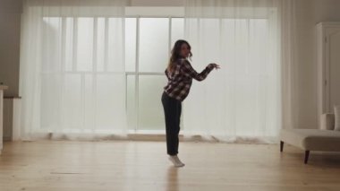 Neşeli hamile bir kadın, sıcak ve rahat bir atmosferle çevrili, aydınlık bir oturma odasında mutlu bir şekilde dans eder.