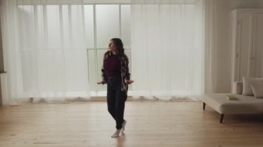Genç bir kadın, aydınlık ve ferah modern oturma odasında tek başına dans etmekten zevk alır..