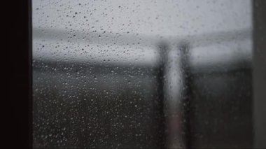 Pencereye yakın plan yağmur damlaları yansıtıcı ve bulanık arkaplanlı karamsar titreşimler. Anahtar sözcükler soyut, ortam, yağmur