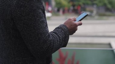Kareli ceketli bir kişi, sonbahar boyunca şehir geçmişi bulanık ve açık havada akıllı telefon kullanıyor.